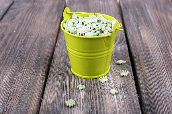 Beads in metal bucket on wooden background