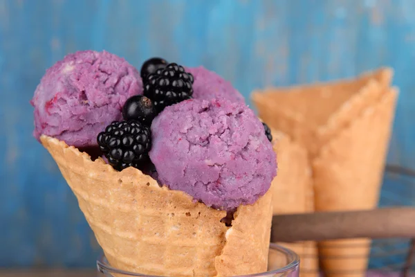 Смачне морозиво з ягодами у вафельному конусі на синьому дерев'яному фоні — стокове фото
