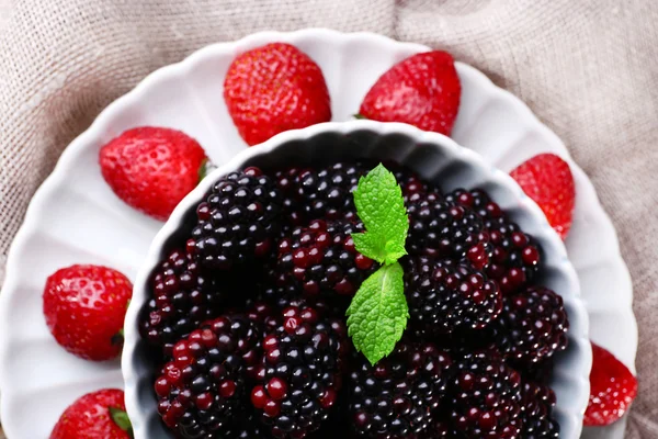 Bowl of blackberries and plate of strawberries on sacking background — Stock Photo, Image