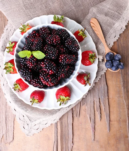 Bowl of blackberries and plate of strawberries on wooden background — Stock Photo, Image