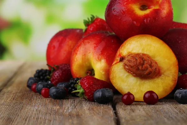 Pesche con bacche sul tavolo su sfondo naturale — Foto Stock