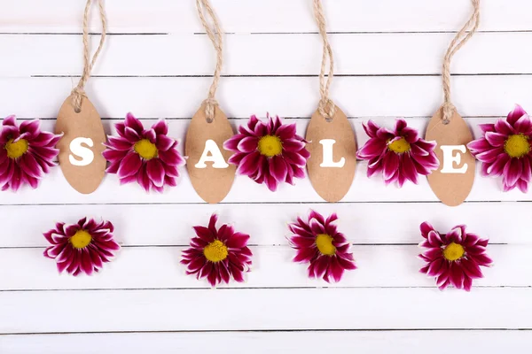 Beautiful chrysanthemum flowers and sale tags on white wooden background — Stock Photo, Image