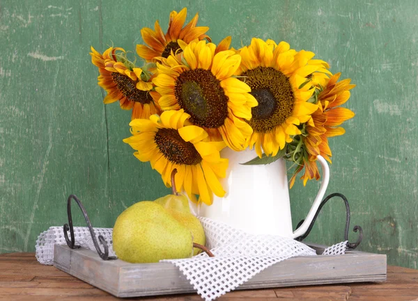 Beautiful sunflowers in pitcher with pears on table on wooden background — Stock Photo, Image