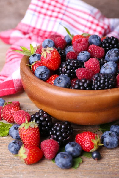 Ripe sweet different berries in bowl, on old wooden table — Stock Photo, Image