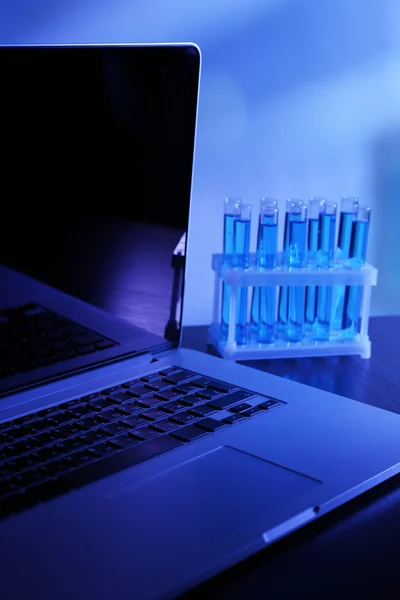 Laptop with test tubes in a laboratory on blue background — Stock Photo, Image