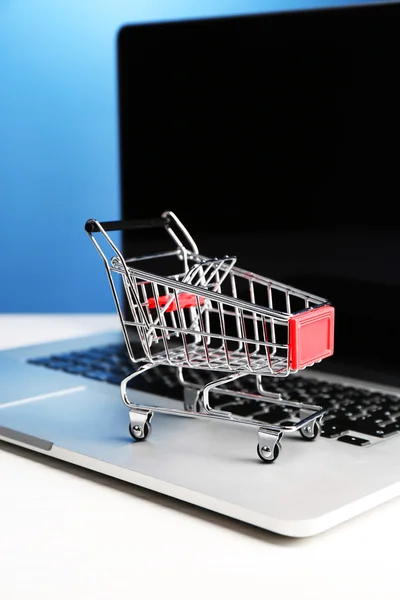 Carro de la compra en el ordenador portátil en la mesa, sobre fondo azul —  Fotos de Stock