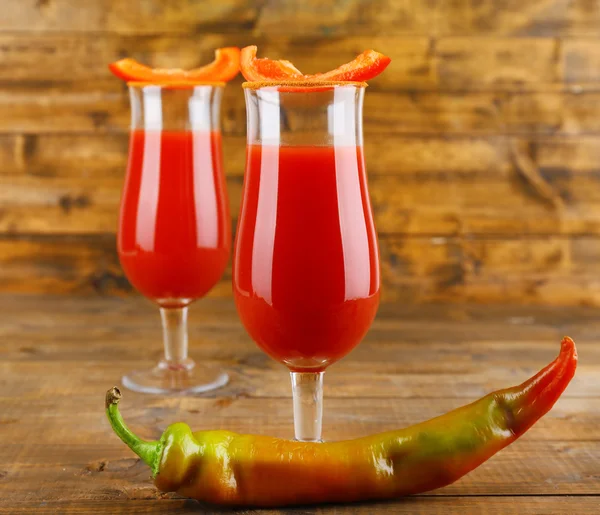 Copos de suco de tomate saboroso e pimenta na mesa de madeira — Fotografia de Stock