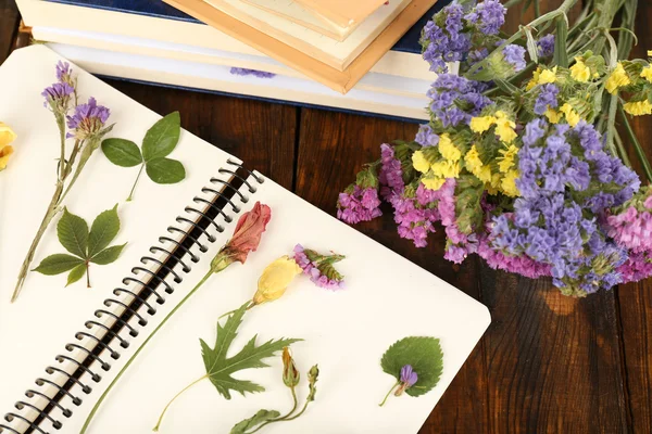 用鲜花和植物在木制的背景上的笔记本上枯竭的组成 — 图库照片