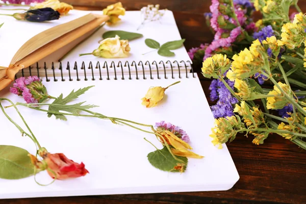 Komposition mit Blumen und vertrockneten Pflanzen auf Notizbüchern auf dem Tisch in Großaufnahme — Stockfoto