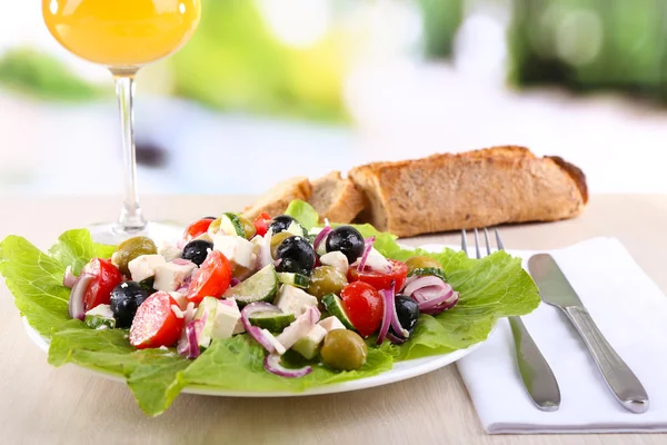 Insalata greca in piatto e bicchiere di vino su tavola di legno su sfondo naturale — Foto Stock