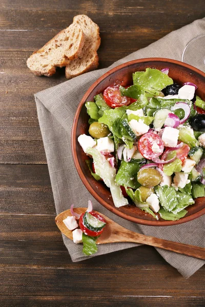 Salada grega servida em tigela com fatia de pão em guardanapo de saque em fundo de madeira — Fotografia de Stock