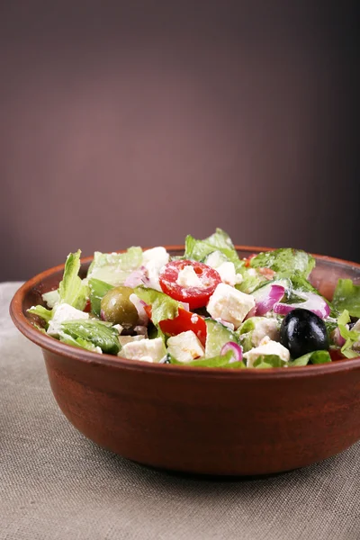 Bowl of Greek salad served on napkin on wooden table on dark background — Stock Photo, Image