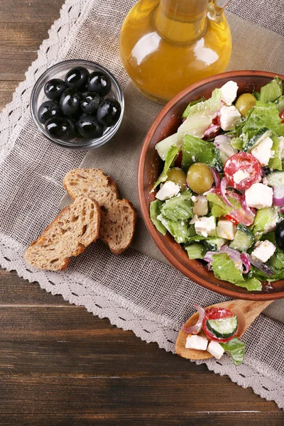 Bowl of Greek salad served with olive oil on sacking napkin on wooden background — Stock Photo, Image