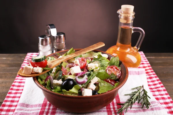 Чаша грецький салат подають з оливковою олією на серветці на дерев'яний стіл на темному тлі — стокове фото