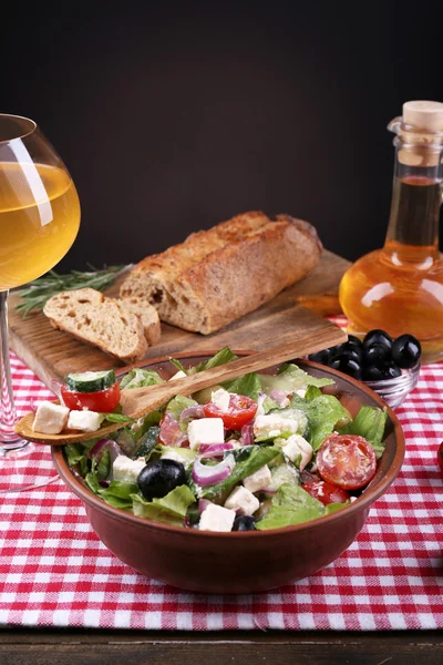 Tigela de salada grega servida com azeite e copo de vinho em guardanapo sobre mesa de madeira sobre fundo escuro — Fotografia de Stock