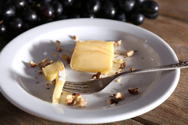 Tasty grape and cheese on plate, on wooden table — Stock Photo, Image