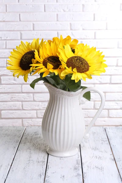 Schöner Strauß Sonnenblumen in Krug auf Tisch auf Backsteinmauer Hintergrund — Stockfoto