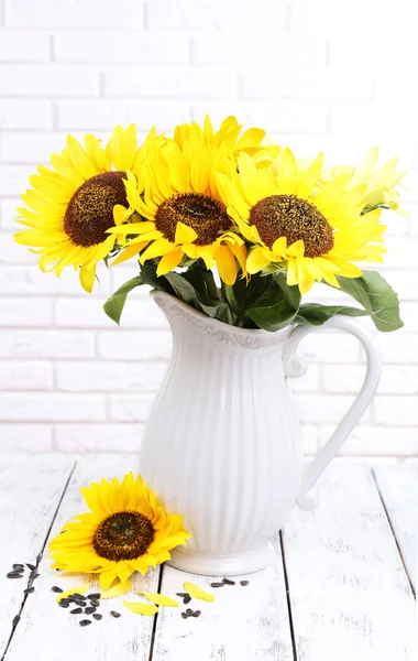 Beautiful bouquet of sunflowers in pitcher on table on brick wall background — Stock Photo, Image