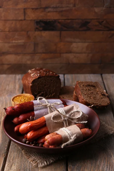 Surtido de salchichas finas y especias en plato, sobre fondo de madera — Foto de Stock