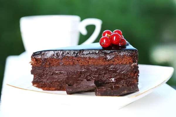 Pastel de chocolate en el plato y taza de té en la mesa, sobre fondo brillante — Foto de Stock