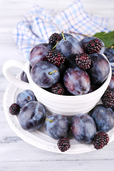 Ripe sweet plums in big cup, on grey wooden table — Stock Photo, Image