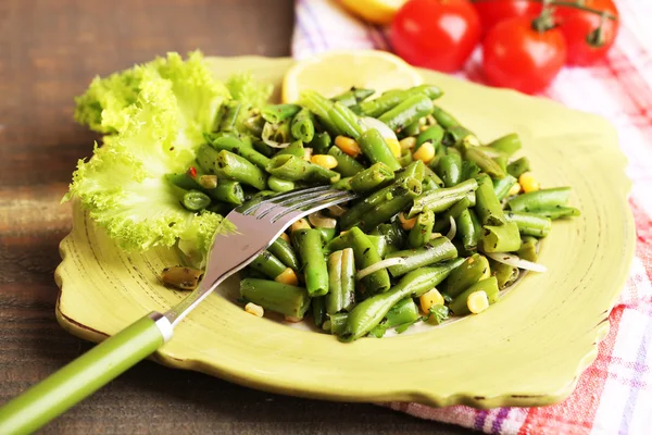 Салат с зеленой фасолью и кукурузой, семена кунжута на тарелке, на фоне цвета дерева — стоковое фото