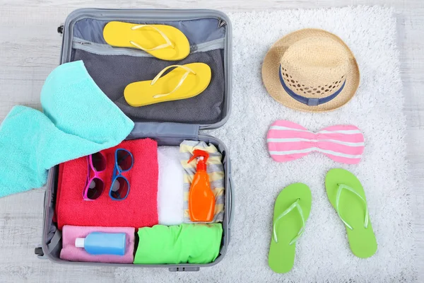 Maleta con cosas en alfombra blanca en el suelo para viajar a algún lugar cerca del agua para pasar las vacaciones de verano —  Fotos de Stock