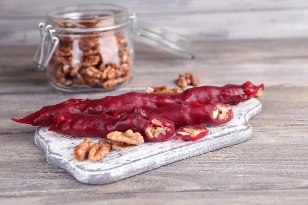 Tasty oriental sweets (churchkhela) and fresh nuts in glass jar, on wooden background — Stock Photo, Image