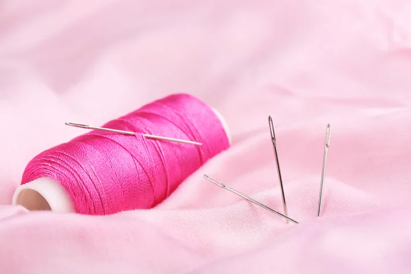 Needles and spool of thread on color fabric background — Stock Photo, Image