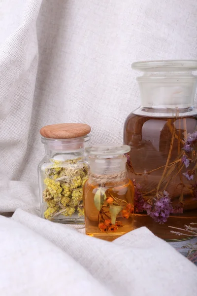 Bottles of herbal tincture and dried herbs on a napkin on wooden background in front of curtain — Stock Photo, Image