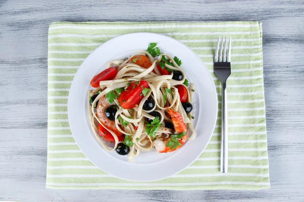 Fresh prawns with spaghetti, olives, tomatoes and parsley in a big round plate on napkin on wooden background — Stock Photo, Image