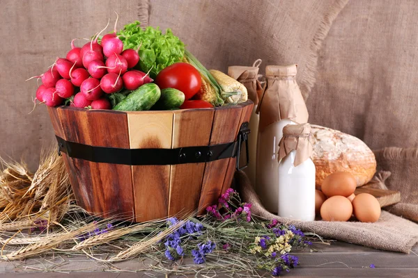 Big round wooden basket with vegetables, milk and bread on sacking background — Stock Photo, Image