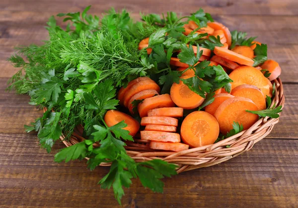 Slices of carrot and parsley in wicker bowl on wooden background — Stock Photo, Image