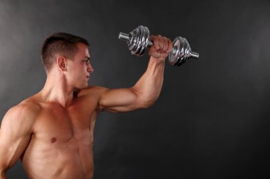 yakışıklı genç kaslı sporcu, koyu arka plan üzerinde egzersiz halter ile yürütmek