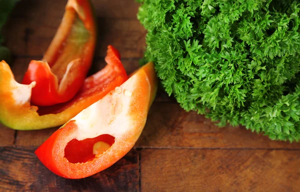 Groene verse peterselie en gesneden paprika op houten achtergrond — Stockfoto