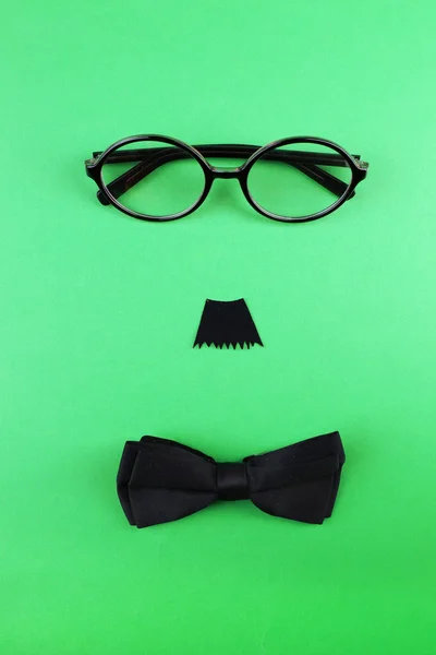 Glasses, mustache and bow tie forming man face on color background — Stock Photo, Image