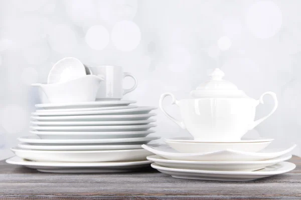 Witte servies en keukengerei, op houten tafel, op lichte achtergrond — Stockfoto