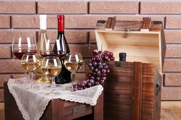 Botellas y vasos de vino y uvas maduras en la mesa sobre fondo de pared de ladrillo — Foto de Stock