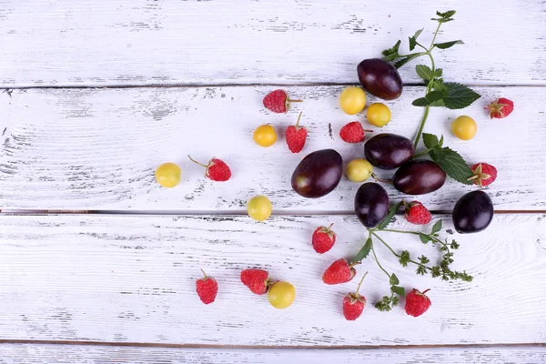 Красивые спелые сливы и ягоды на деревянном столе крупным планом — стоковое фото