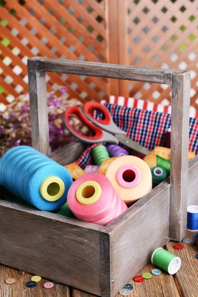 Accesorios de costura en caja de madera sobre mesa sobre fondo marrón —  Fotos de Stock