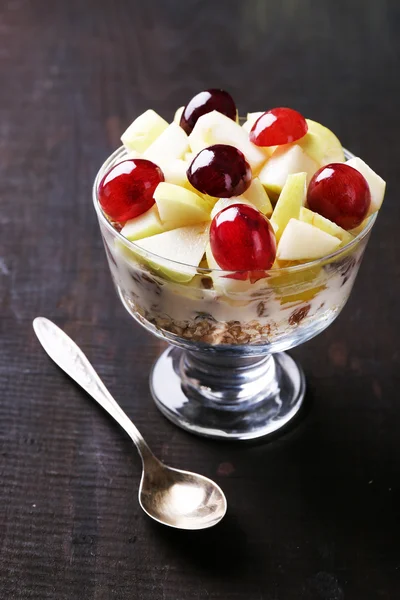 Gezond ontbijt - yoghurt met vers druif en apple segmenten en muesli geserveerd in glazen kom, op houten achtergrond — Stockfoto