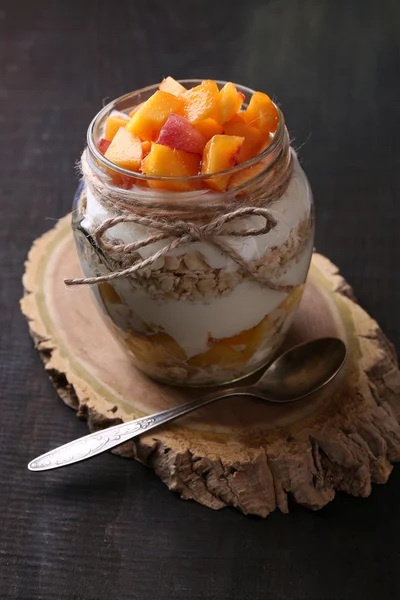 Здоровий сніданок - йогурт зі свіжим персиком та мюслі, поданий у скляній банці, на дерев'яному фоні — стокове фото