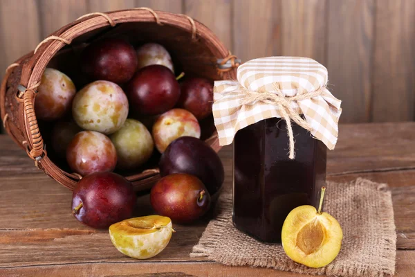 Tasty plum jam in jar and plums on wooden table on wooden background