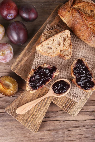 Bröd med plommon sylt och plommon på träbord närbild — Stockfoto