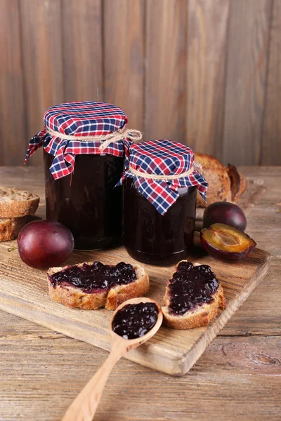 Smakelijke pruim jam in potten en pruimen op houten tafel — Stockfoto