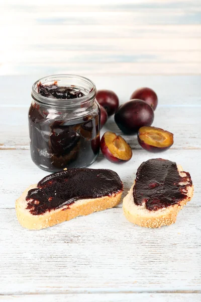 Bread with plum jam and plums on wooden table — Stock Photo, Image