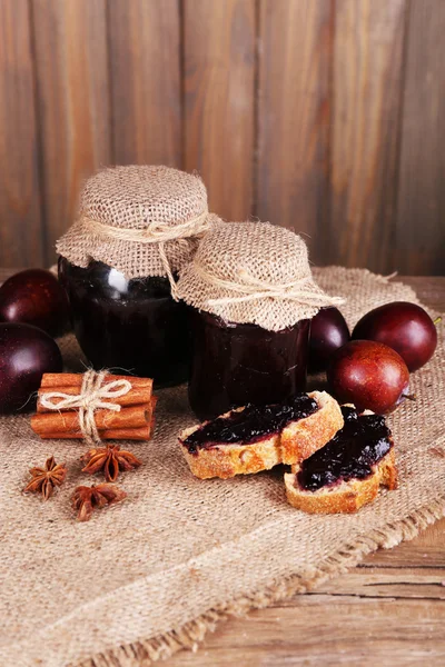 Tasty plum jam in jars and plums on wooden table on wooden background — Stock Photo, Image