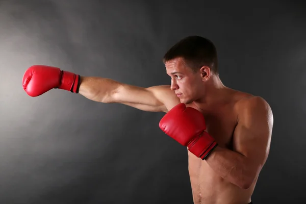 Bello giovane sportivo muscoloso con guanti da boxe su sfondo scuro — Foto Stock