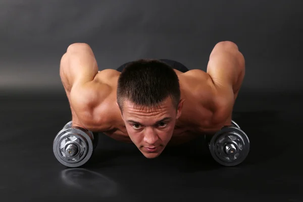 Schöner junger muskulöser Sportler führt Übungen mit Kurzhanteln auf dunklem Hintergrund aus — Stockfoto