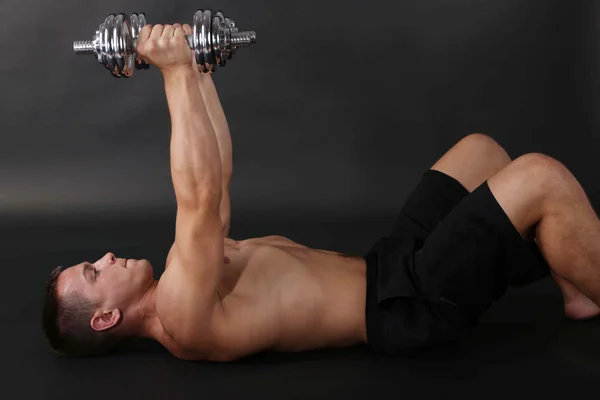 Schöner junger muskulöser Sportler führt Übungen mit Kurzhanteln auf dunklem Hintergrund aus — Stockfoto